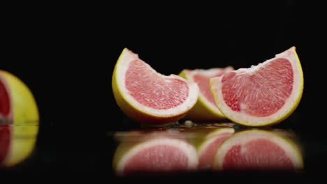 Red-juicy-sliced-​​grapefruit-falling-on-a-glass-with-splashes-of-water-in-slow-motion-on-a-dark-background